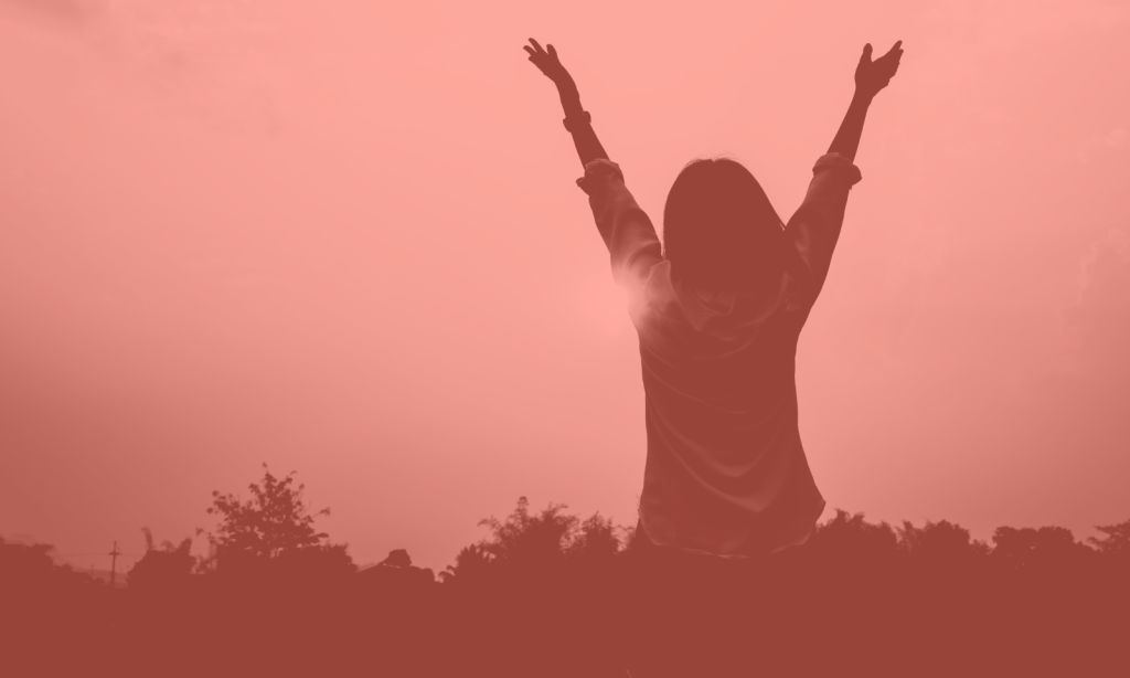 silhouette of a woman raising her arms in joy looking at the sunset