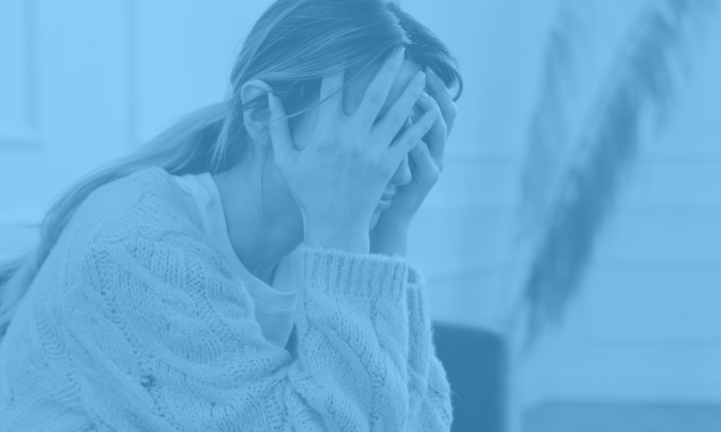 Woman sitting with her hands over her face struggling with feeling overwhelmed or stressed